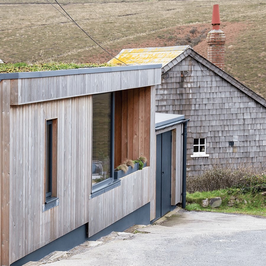 modern timber clad building against a traditional Cornish mining cottage