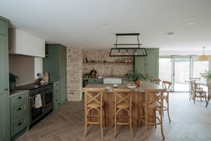 open plan kitchen with green units and bare stone wall