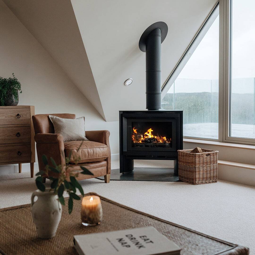 Marraum — lit wood burner with brown chair next to it and large window