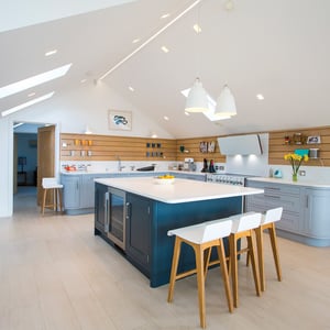 large kitchen island with white worktop and dark blue units and three white bar stools