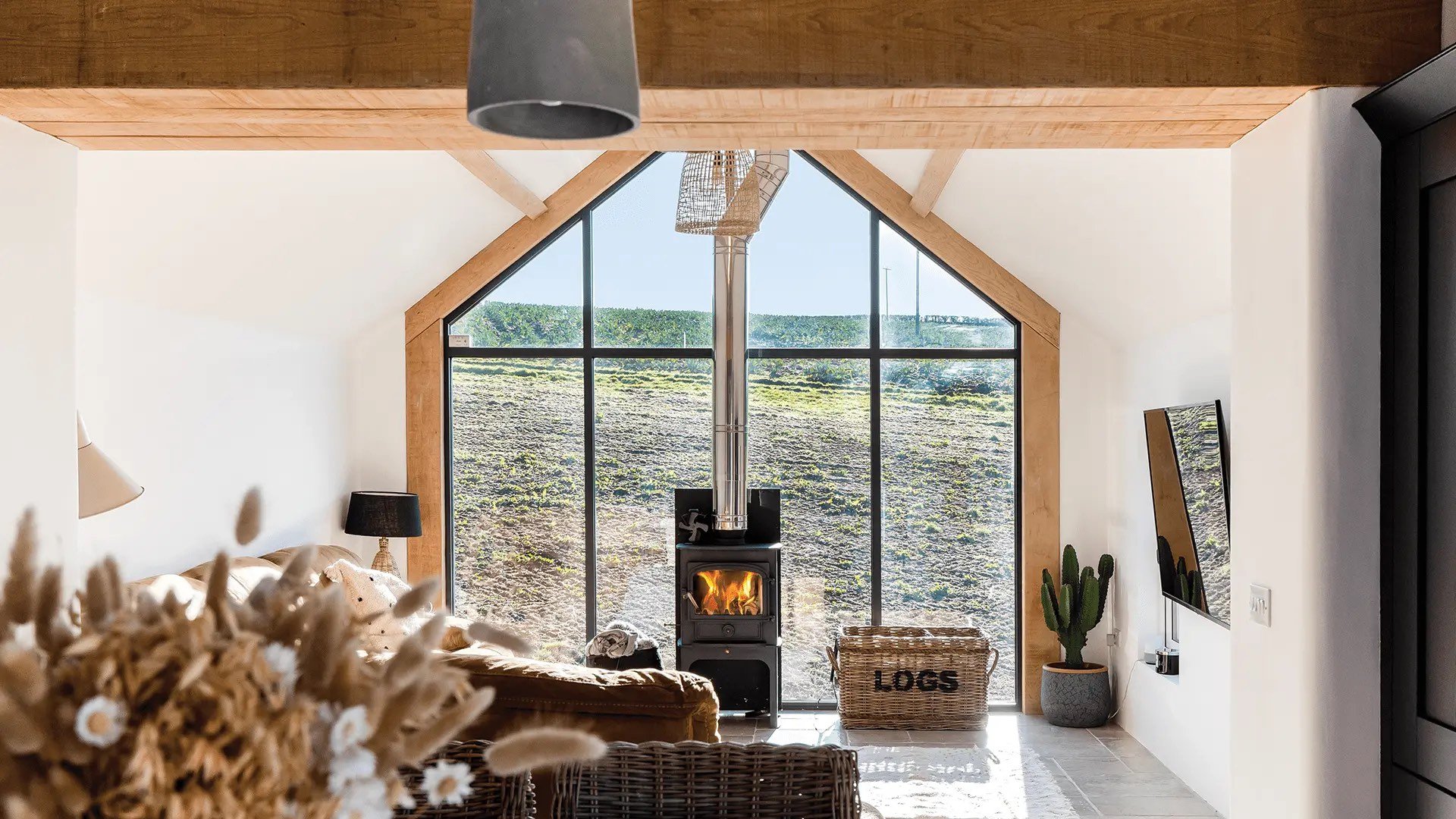 Internal view of woodburner in front of large gable window looking out towards countryside