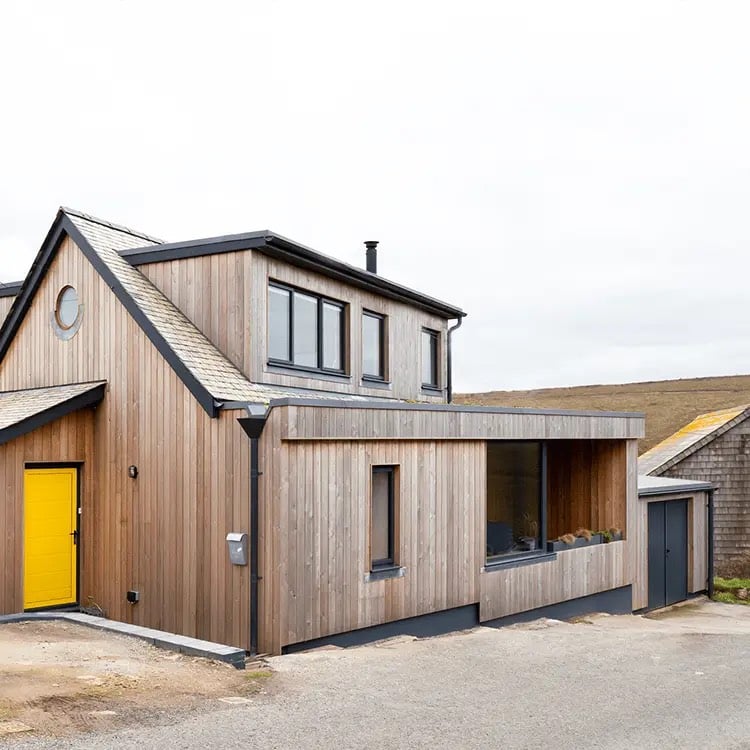 external view of a timber clad dormer bungalow with bright yellow door